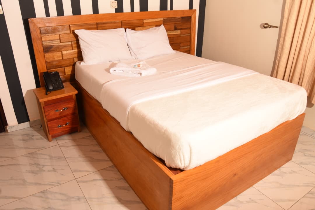 Lit double avec linge blanc, table de chevet et mur rayé noir et blanc